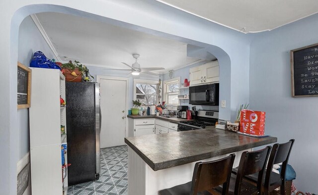 kitchen featuring dark countertops, appliances with stainless steel finishes, arched walkways, a peninsula, and white cabinetry