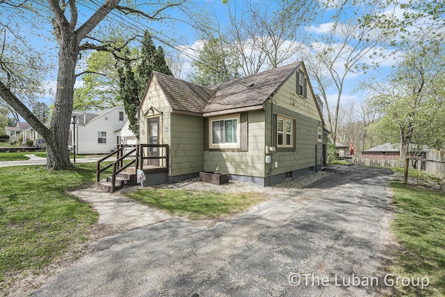 view of front facade featuring fence, a shingled roof, a front yard, and aphalt driveway