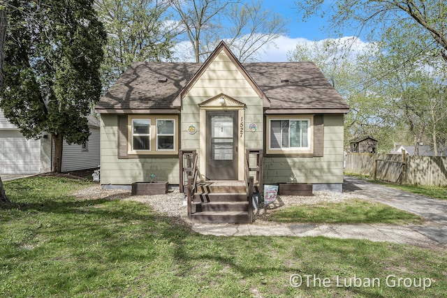 view of front of house with fence, roof with shingles, and a front yard