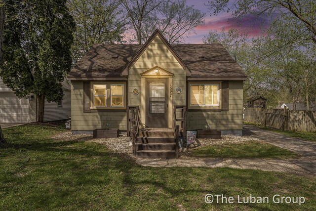view of front of home with entry steps, fence, a shingled roof, and a front yard