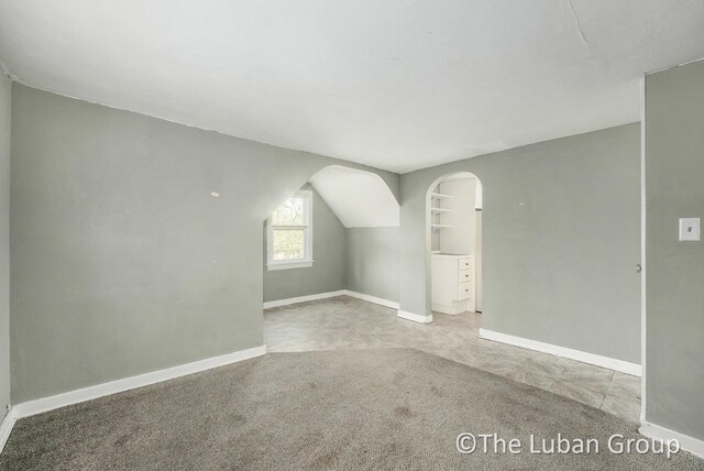 additional living space with baseboards, carpet flooring, and arched walkways