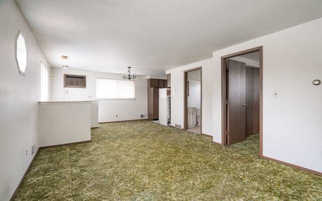 carpeted empty room featuring visible vents, baseboards, a chandelier, and a wall mounted AC