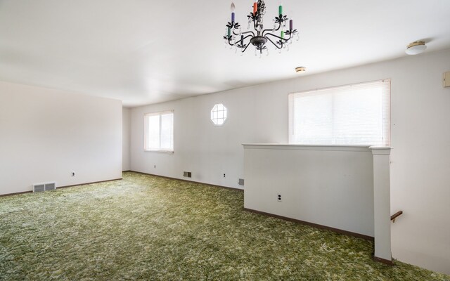 carpeted empty room featuring baseboards, visible vents, and an inviting chandelier