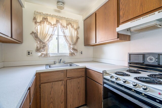kitchen with light countertops, electric range oven, under cabinet range hood, brown cabinets, and a sink