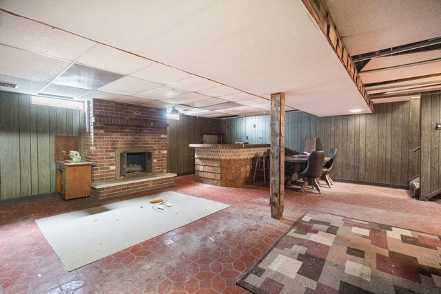 finished basement featuring wooden walls, a dry bar, a brick fireplace, and a paneled ceiling