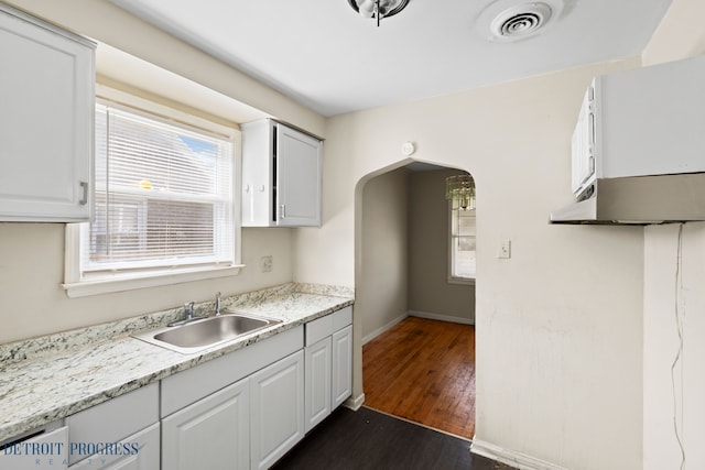 18626 Prevost St, Detroit, MI 48235 - kitchen with dark wood-style flooring, arched walkways, a sink, baseboards, and white cabinetry