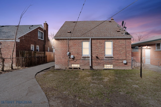 18626 Prevost St, Detroit, MI 48235 - back of property at dusk with a yard, brick siding, fence, and roof with shingles