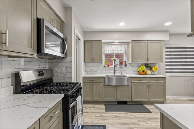 kitchen with light stone countertops, appliances with stainless steel finishes, a sink, light wood-type flooring, and tasteful backsplash