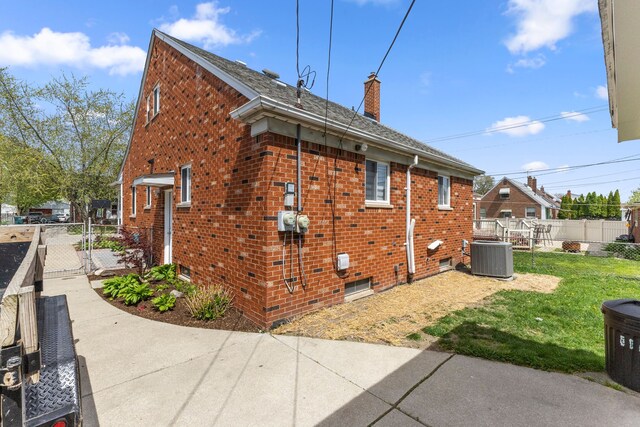 exterior space with a chimney, central air condition unit, brick siding, fence, and a yard