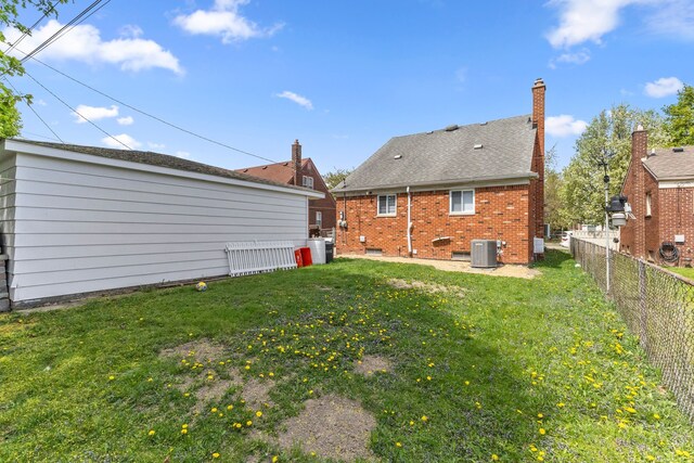 rear view of house with a chimney, a lawn, central AC unit, brick siding, and a fenced backyard