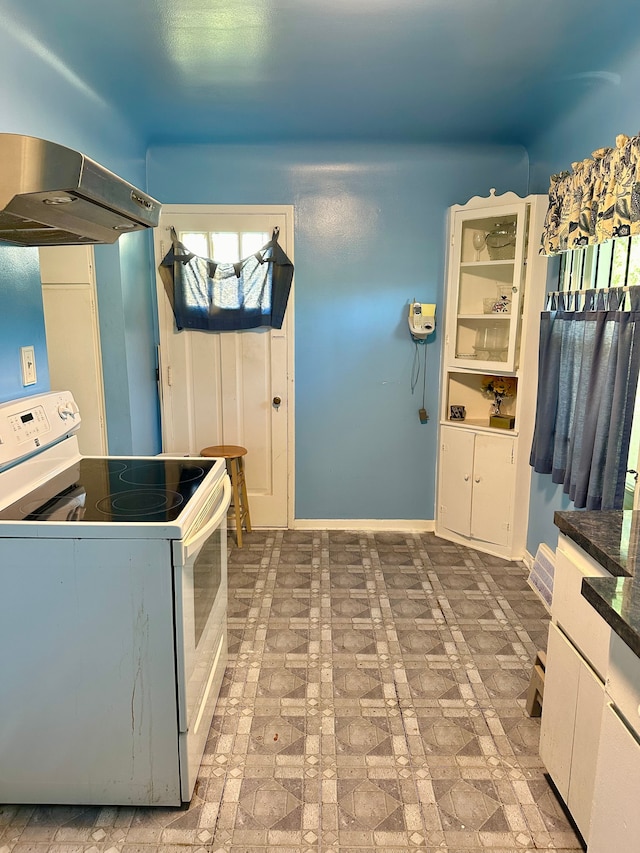 kitchen with brick patterned floor, dark countertops, baseboards, under cabinet range hood, and electric stove