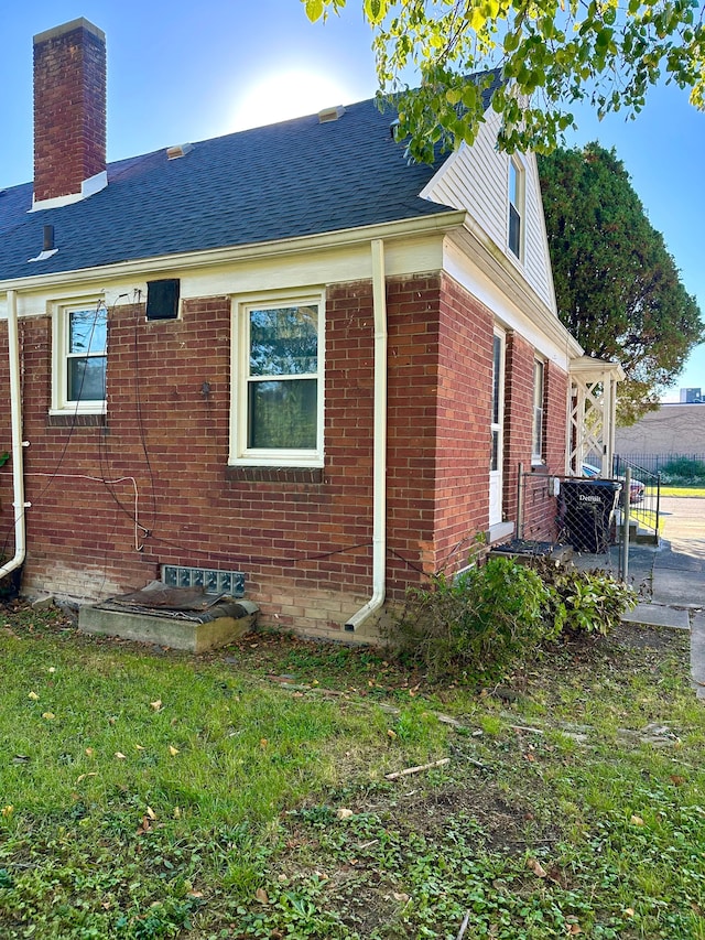 view of side of property featuring a chimney, roof with shingles, a lawn, a patio area, and brick siding