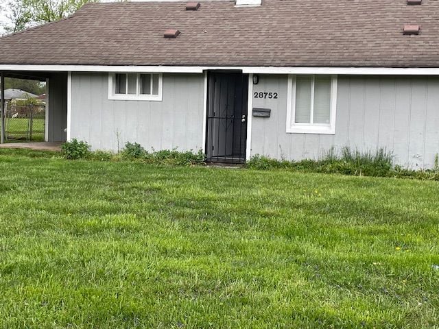entrance to property with roof with shingles and a lawn