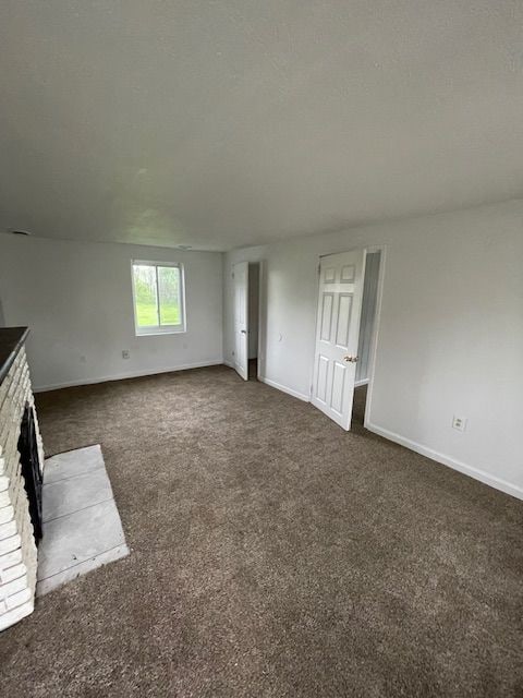 unfurnished living room featuring baseboards, dark colored carpet, and a fireplace
