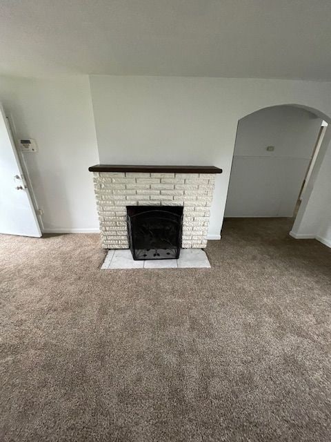 unfurnished living room with carpet flooring, a brick fireplace, arched walkways, and baseboards