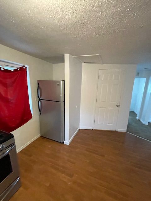 kitchen with stainless steel appliances, a textured ceiling, wood finished floors, and baseboards