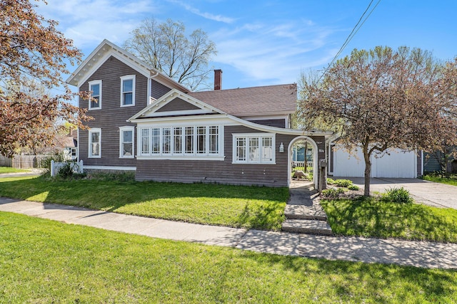 view of front facade with concrete driveway, a chimney, a shingled roof, and a front yard
