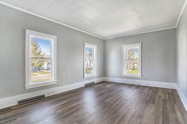 empty room featuring baseboards, visible vents, ornamental molding, and dark wood finished floors