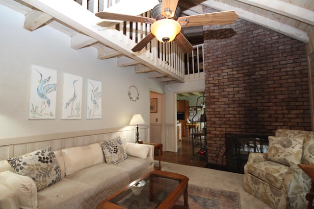 living area with a ceiling fan, brick wall, a fireplace, wainscoting, and beamed ceiling