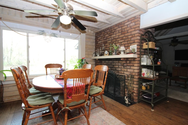dining area featuring hardwood / wood-style floors, ceiling fan, a brick fireplace, and beam ceiling