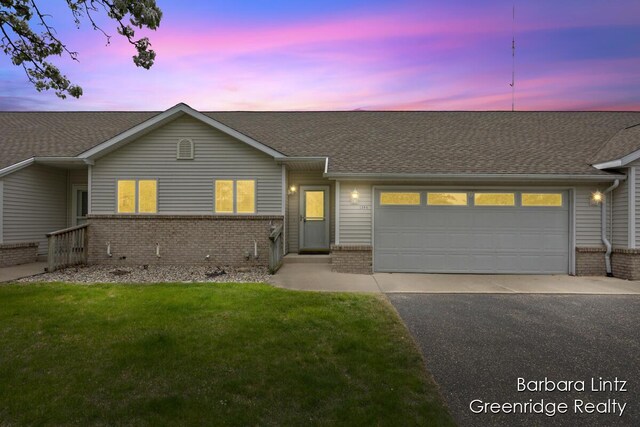 single story home with aphalt driveway, brick siding, a shingled roof, an attached garage, and a yard
