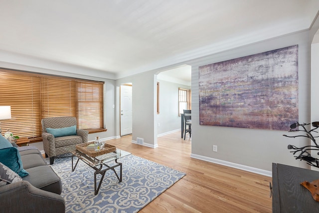living area with light wood-style floors, arched walkways, baseboards, and visible vents