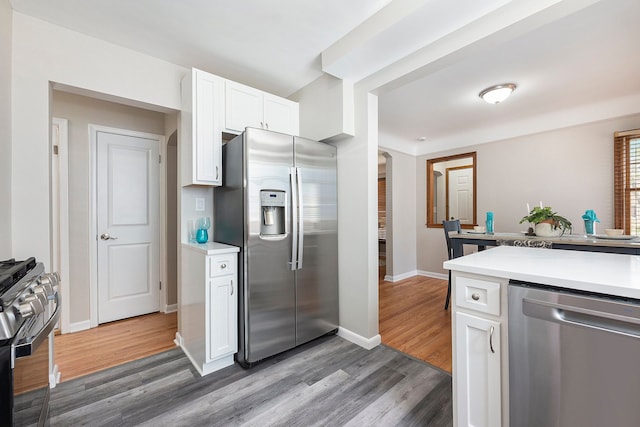 kitchen with appliances with stainless steel finishes, light countertops, arched walkways, white cabinetry, and wood finished floors