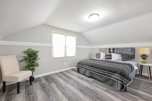 bedroom featuring baseboards, wood finished floors, and lofted ceiling