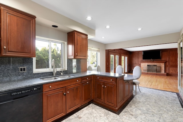 kitchen with a stone fireplace, tasteful backsplash, dishwasher, a sink, and a peninsula