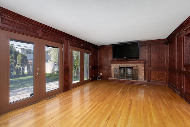 unfurnished living room featuring visible vents, wood walls, a fireplace, french doors, and light wood finished floors