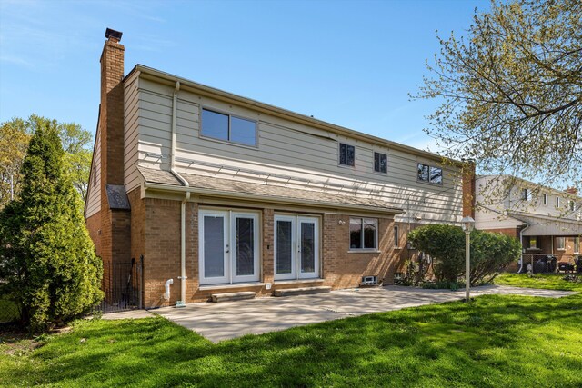 back of house featuring a yard, brick siding, french doors, and a chimney