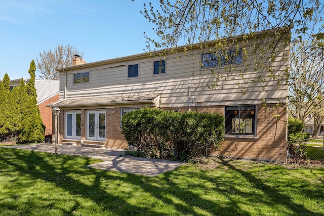 rear view of house with a chimney, french doors, a lawn, brick siding, and a patio