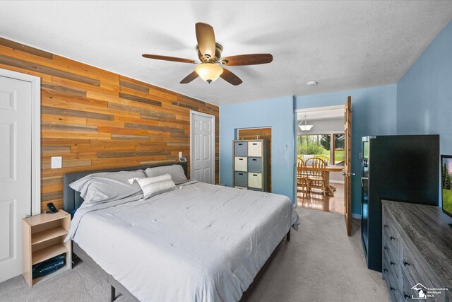 bedroom featuring wood walls, a ceiling fan, an accent wall, and light carpet