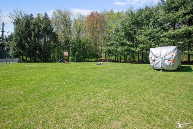 view of yard with a playground, fence, and an outdoor fire pit