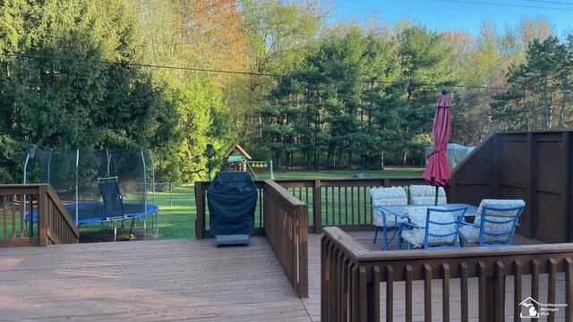 wooden deck featuring outdoor dining area, a trampoline, and a yard