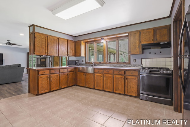 4334 Brunswick Rd, Holton, MI 49425 - kitchen with gas range oven, stainless steel microwave, under cabinet range hood, brown cabinetry, and a peninsula