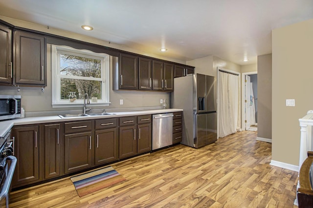 kitchen with appliances with stainless steel finishes, dark brown cabinets, a sink, light countertops, and light wood-style floors