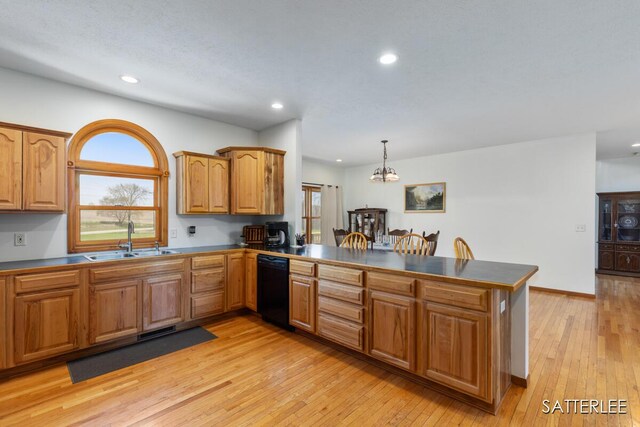 kitchen featuring dark countertops, dishwasher, a sink, a peninsula, and light wood-style floors