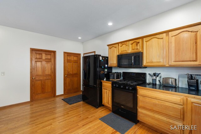 kitchen featuring dark countertops, baseboards, light wood-type flooring, recessed lighting, and black appliances