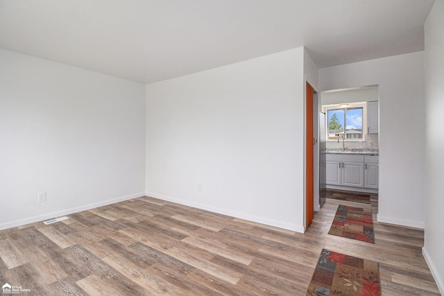 spare room featuring visible vents, a sink, light wood finished floors, and baseboards
