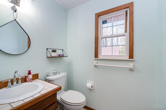 half bathroom featuring toilet, baseboards, and vanity
