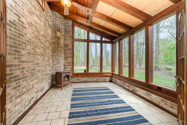 unfurnished sunroom with tile patterned flooring, lofted ceiling with beams, brick wall, and a wealth of natural light