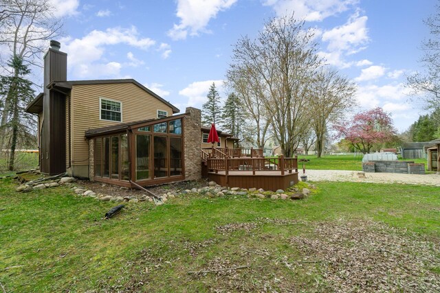 rear view of house with a lawn, a chimney, a sunroom, and a wooden deck