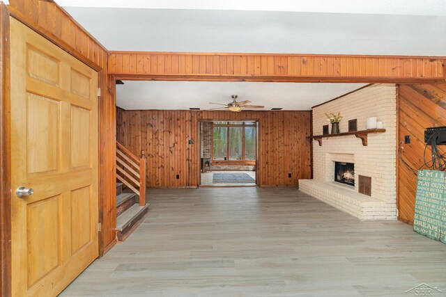 unfurnished living room featuring light wood-style floors, a fireplace, wooden walls, and stairway