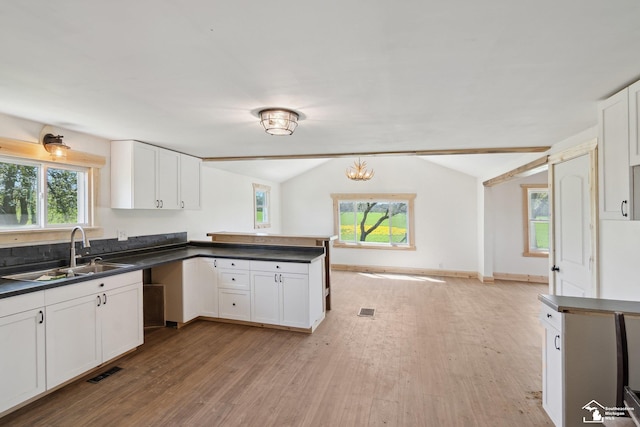 13280 Burt Rd, Pittsford, MI 49271 - kitchen with dark countertops, vaulted ceiling, a sink, light wood finished floors, and white cabinetry