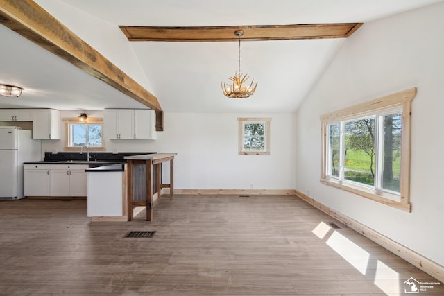 13280 Burt Rd, Pittsford, MI 49271 - kitchen with dark countertops, a notable chandelier, freestanding refrigerator, white cabinetry, and beamed ceiling