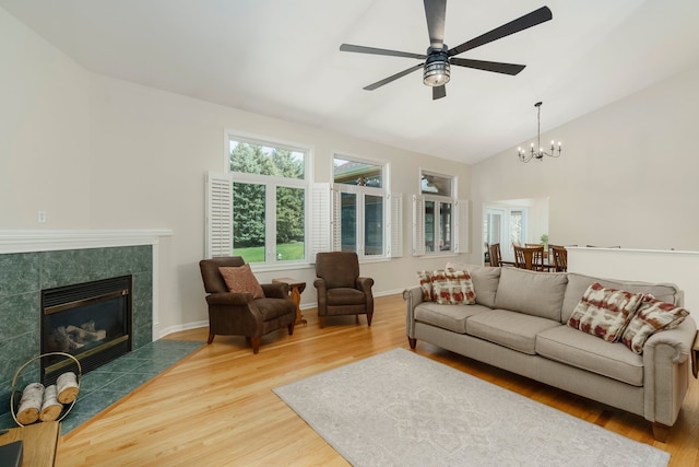 living area featuring ceiling fan with notable chandelier, wood finished floors, high vaulted ceiling, and a tile fireplace