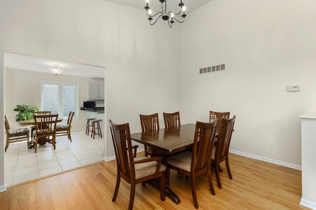 dining area with a towering ceiling, visible vents, light wood-type flooring, baseboards, and a chandelier