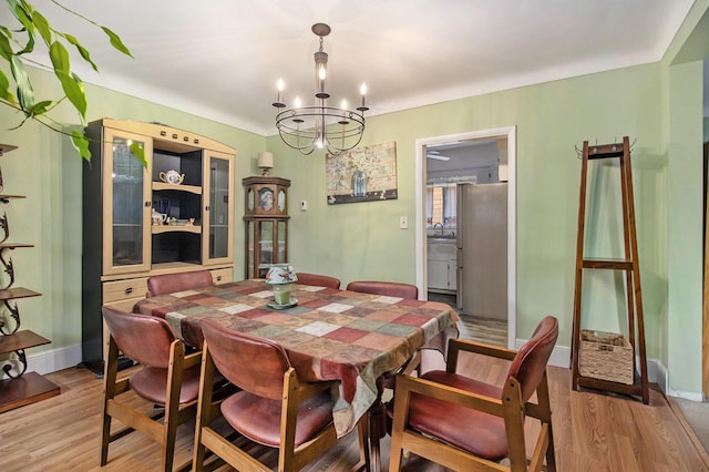 dining space with an inviting chandelier, baseboards, and light wood-style flooring