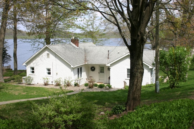 view of front of property with a shingled roof, a front lawn, and a chimney